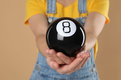 Woman holding magic eight ball on light brown background, closeup