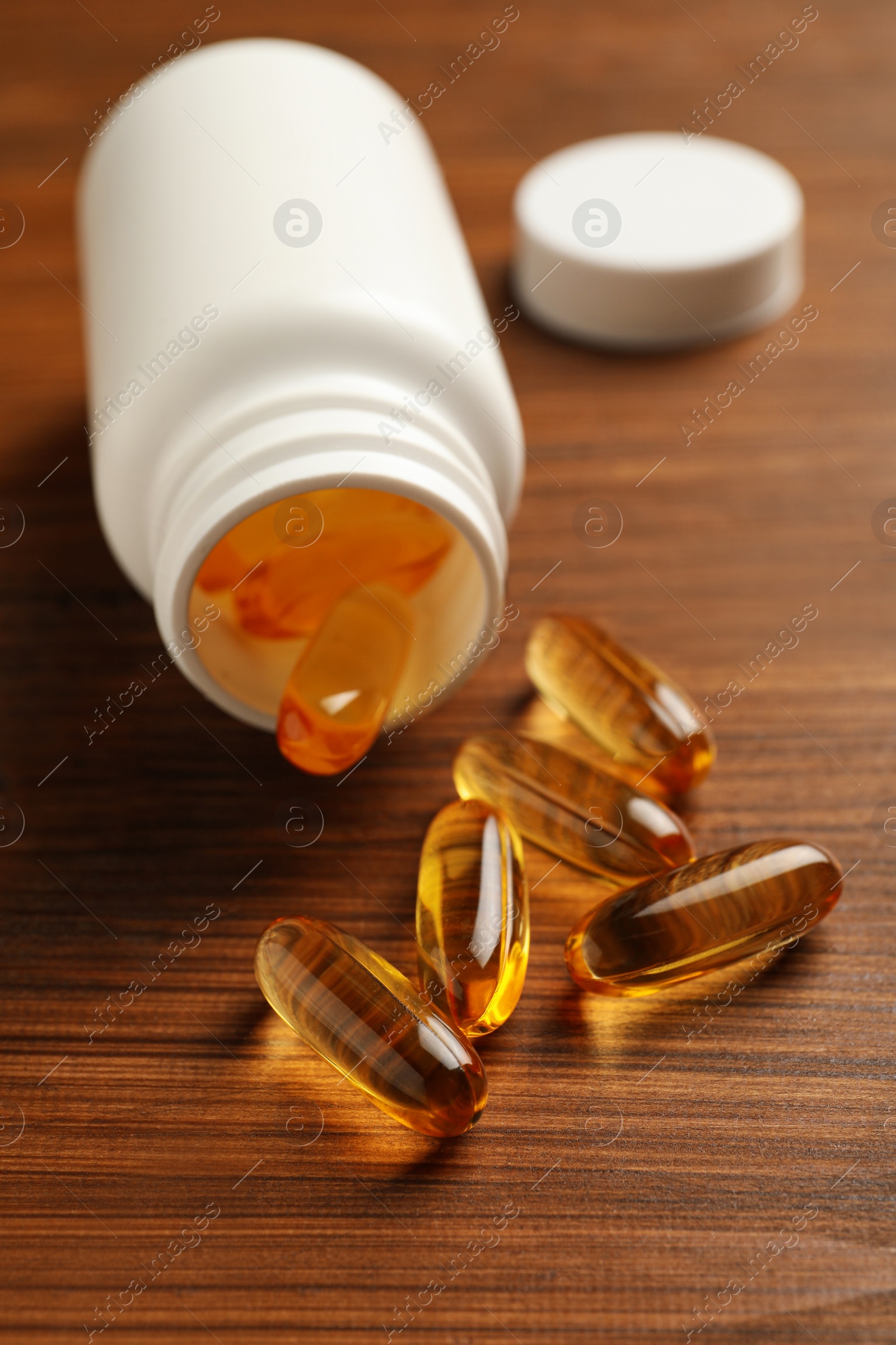 Photo of Overturned bottle with dietary supplement capsules on wooden table