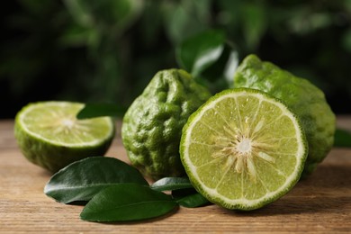 Photo of Fresh ripe bergamot fruits with green leaves on wooden table against blurred background