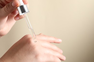 Photo of Woman applying cosmetic serum onto hand on beige background, closeup. Space for text