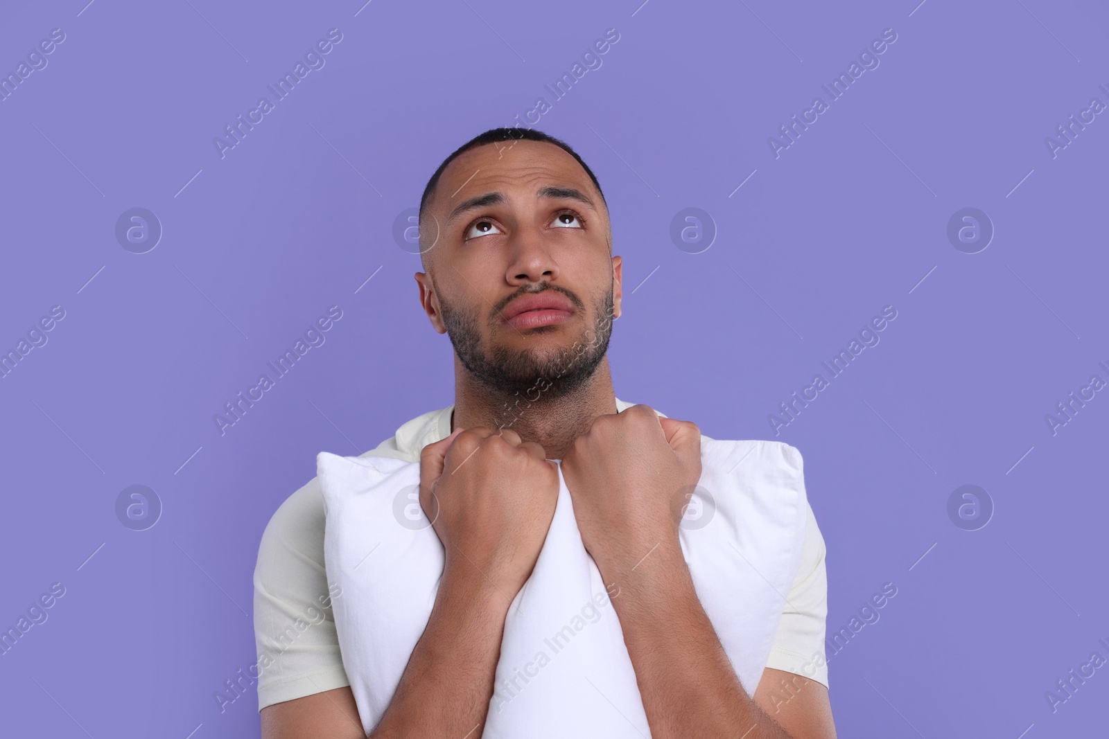 Photo of Tired man with pillow on violet background. Insomnia problem