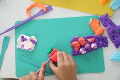 Photo of Little girl sculpting with play dough at white table, top view