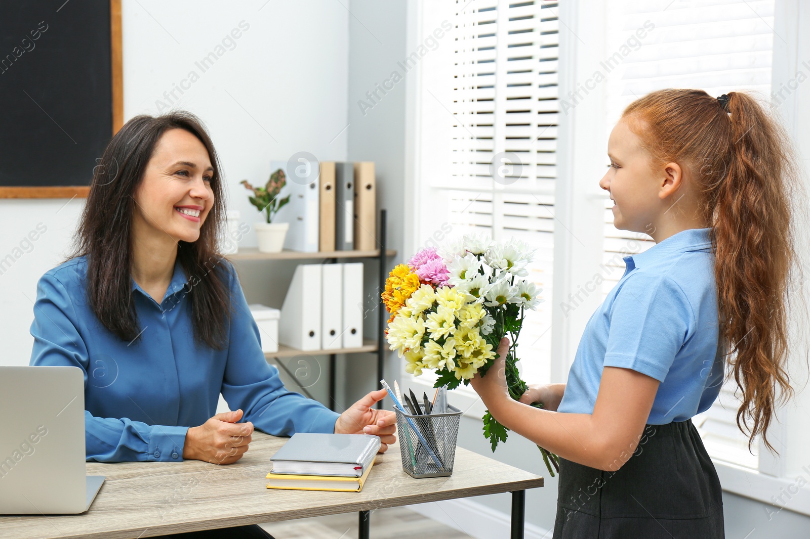 Photo of Schoolgirl with bouquet congratulating her pedagogue in classroom. Teacher's day