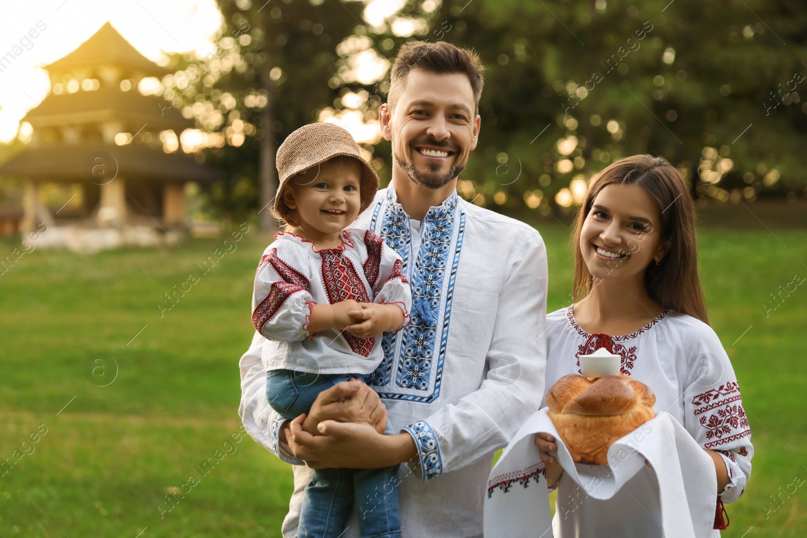 Photo of Happy cute family in embroidered Ukrainian shirts with korovai bread on sunny day. Space for text