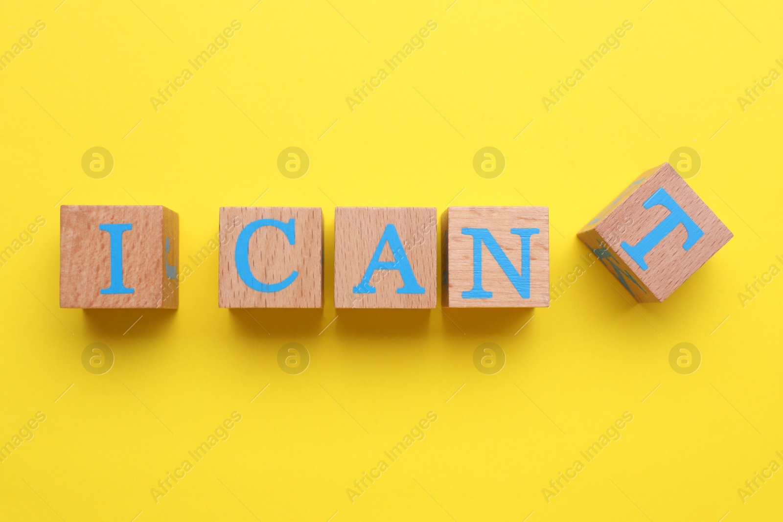 Photo of Motivation concept. Changing phrase from I Can't into I Can by removing cube with letter T on yellow background, top view