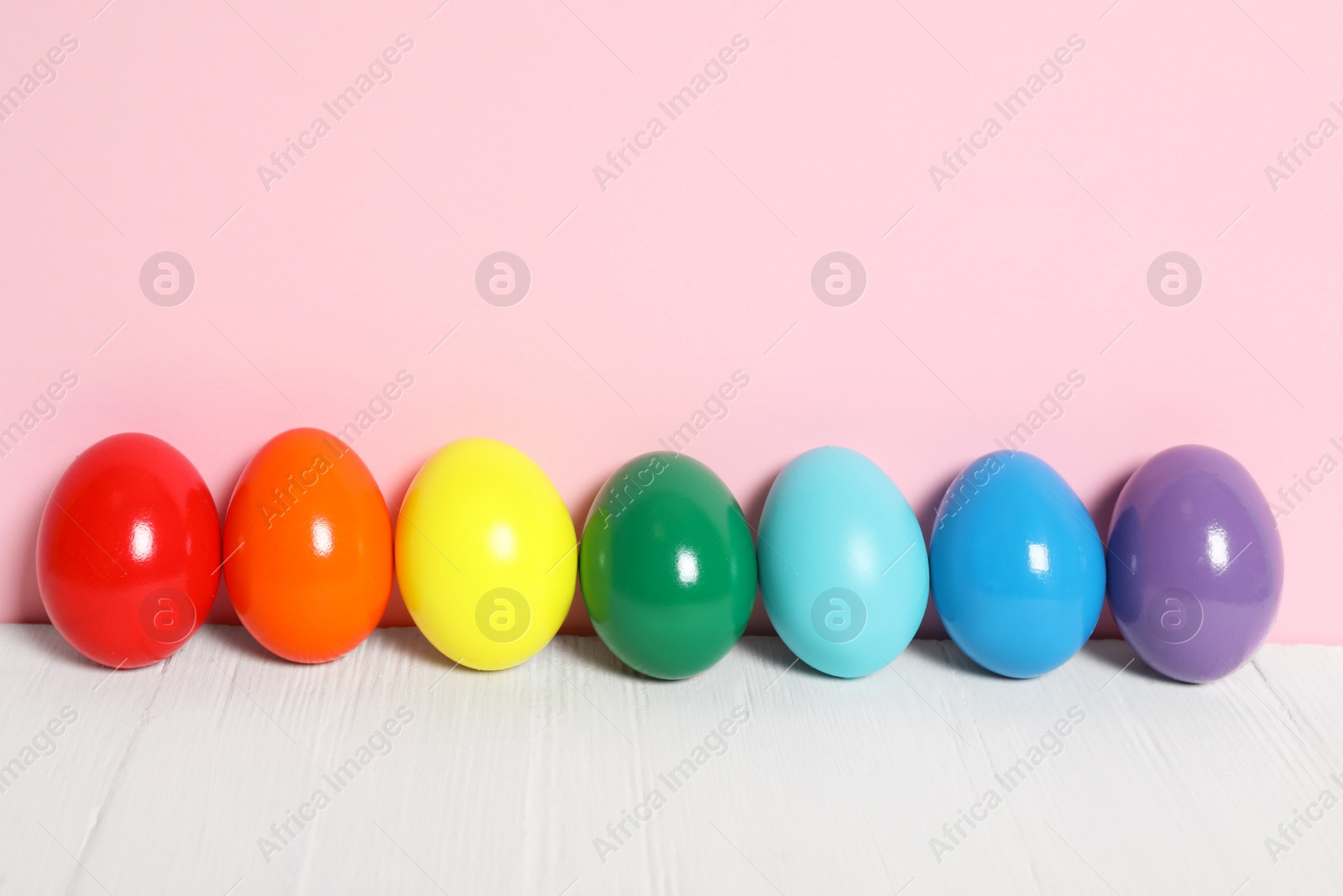 Photo of Easter eggs on white wooden table against pink background, space for text