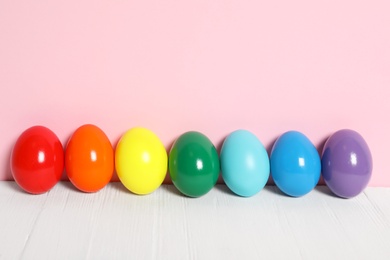 Easter eggs on white wooden table against pink background, space for text