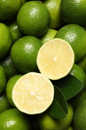 Fresh limes and leaves with water drops as background, top view