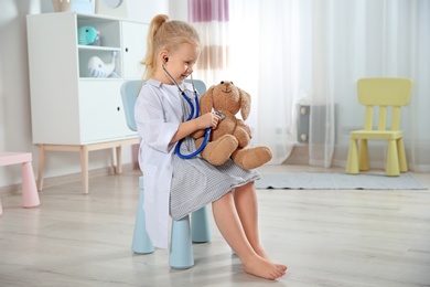 Photo of Cute child imagining herself as doctor while playing with stethoscope and toy bunny at home