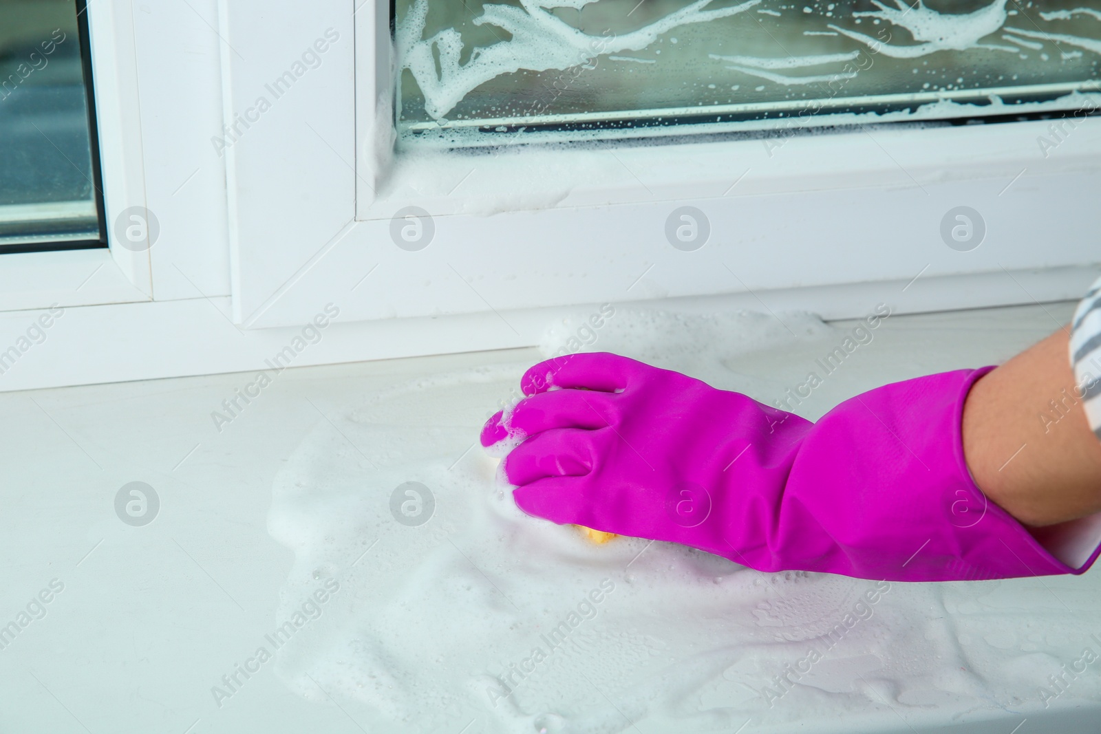 Photo of Woman cleaning window sill with sponge indoors, closeup