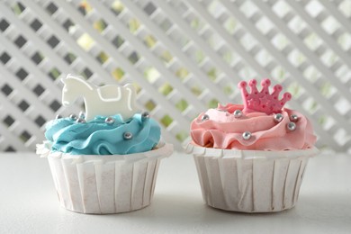 Photo of Delicious cupcakes with pink and light blue cream for baby shower on white table