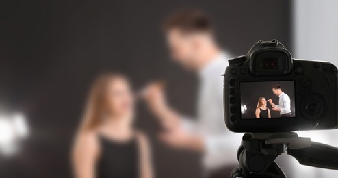 Professional makeup artist working with beautiful young woman in photo studio, selective focus on camera display