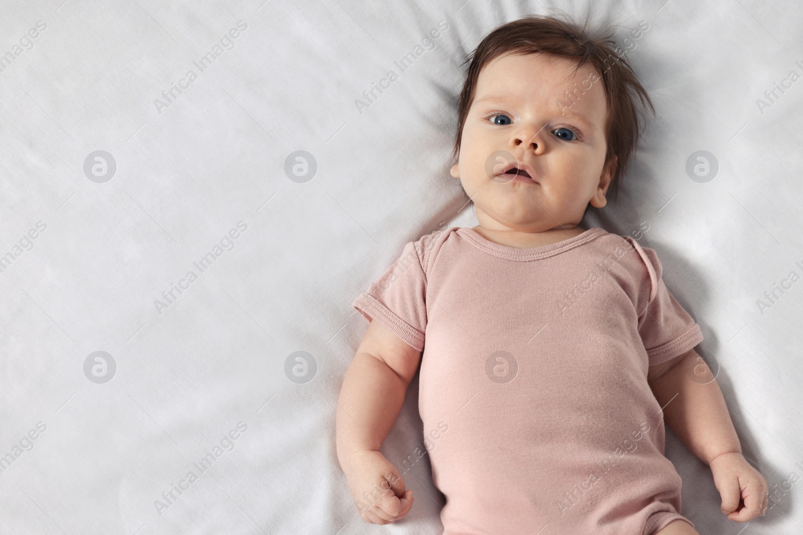 Photo of Cute little baby on cosy bed, top view. Space for text