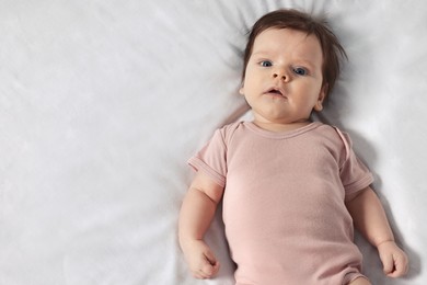 Photo of Cute little baby on cosy bed, top view. Space for text