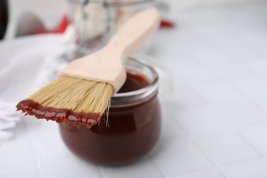 Photo of Marinade in jar and basting brush on white table, closeup. Space for text