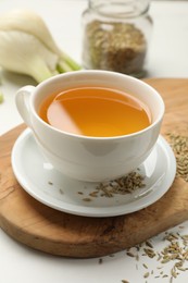 Fennel tea in cup, seeds and fresh vegetable on white table, closeup