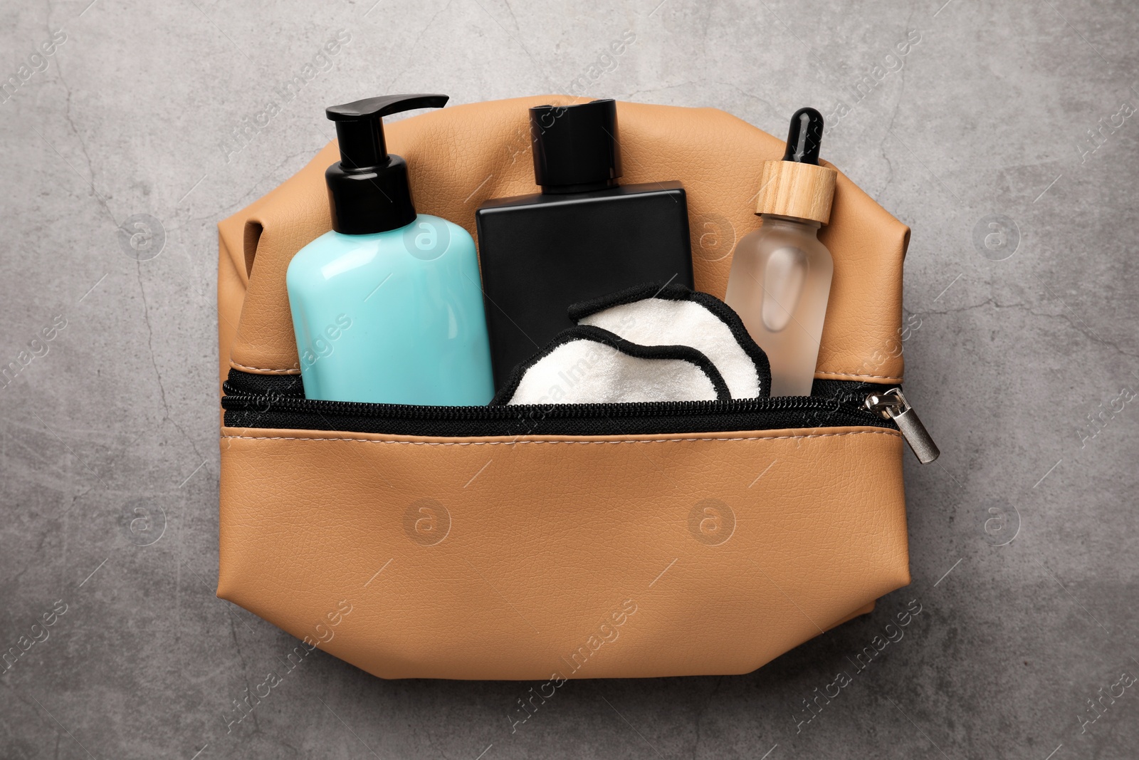 Photo of Preparation for spa. Compact toiletry bag with different cosmetic products on grey textured background, top view