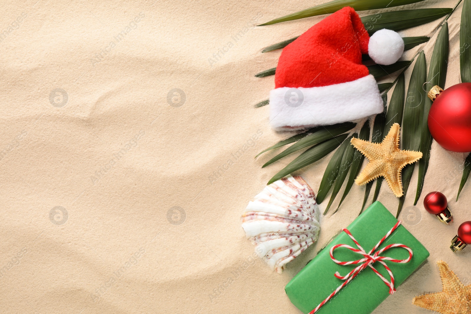 Photo of Flat lay composition with Santa hat and starfishes on sand, space for text. Christmas vacation