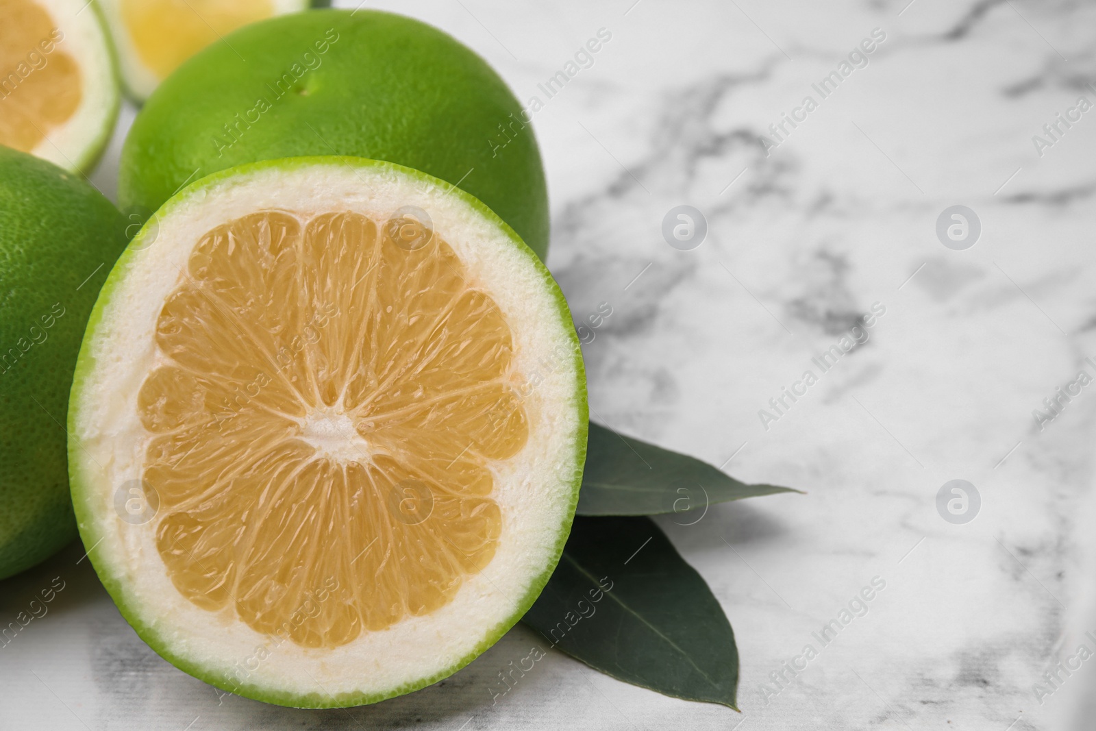 Photo of Whole and cut sweetie fruits with green leaves on white marble table, closeup. Space for text