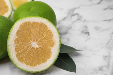 Photo of Whole and cut sweetie fruits with green leaves on white marble table, closeup. Space for text