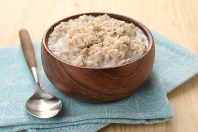 Photo of Tasty boiled oatmeal in bowl and spoon on wooden table, closeup