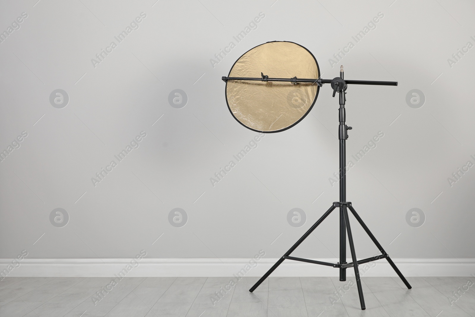 Photo of Studio reflector on tripod near grey wall in room, space for text. Professional photographer's equipment