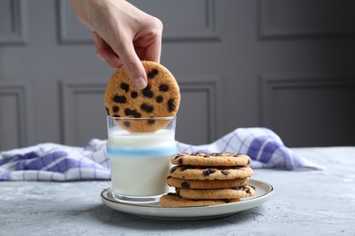 Photo of Woman dipping delicious chocolate chip cookie into glass of milk at grey textured table, closeup