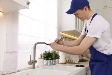 Young plumber examining metal faucet in kitchen
