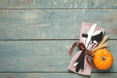 Top view of cutlery with napkin, wheat spikes and pumpkin on blue wooden table, space for text. Thanksgiving Day