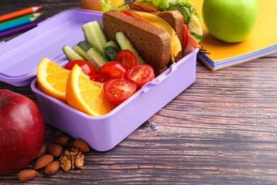 Lunch box with healthy food for schoolchild and different stationery on wooden table, closeup. Space for text