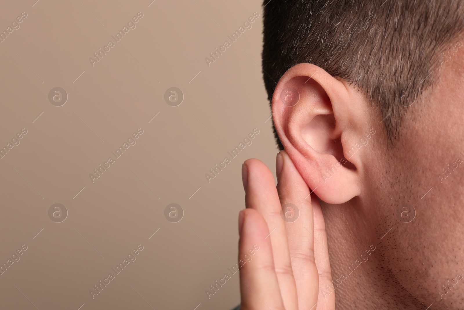 Photo of Man showing hand to ear gesture on beige background, closeup. Space for text