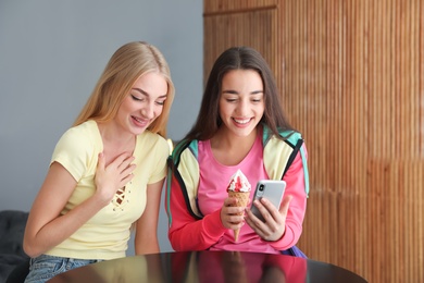 Young women with ice cream and smartphone laughing together indoors