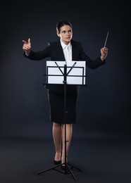 Professional conductor with baton and note stand on dark background