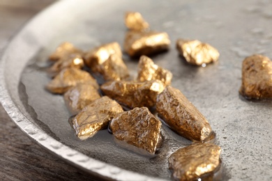 Photo of Plate with gold nuggets and water on table, closeup