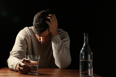 Addicted man with alcoholic drink at wooden table against black background, focus on glass
