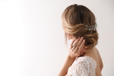 Photo of Young bride with elegant wedding hairstyle on light background, back view. Space for text