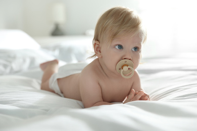 Photo of Cute little baby in diaper with pacifier lying on bed at home