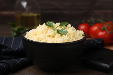 Tasty couscous and fresh parsley in bowl on table, closeup