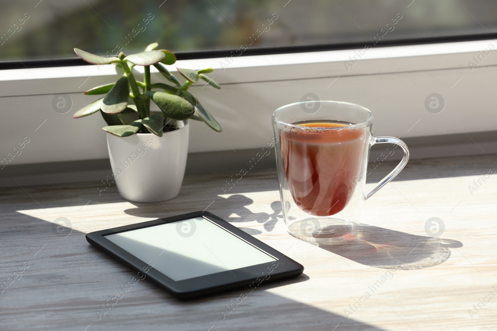 Photo of Cup of tea, e-book reader and houseplant on wooden window sill