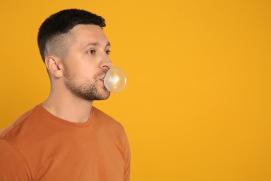 Photo of Handsome man blowing bubble gum on orange background, space for text