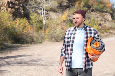 Photo of Young male camper with sleeping bag in wilderness. Space for text