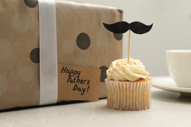 Photo of Delicious cupcake with mustache topper, present and card with phrase Happy Father's Day on light table