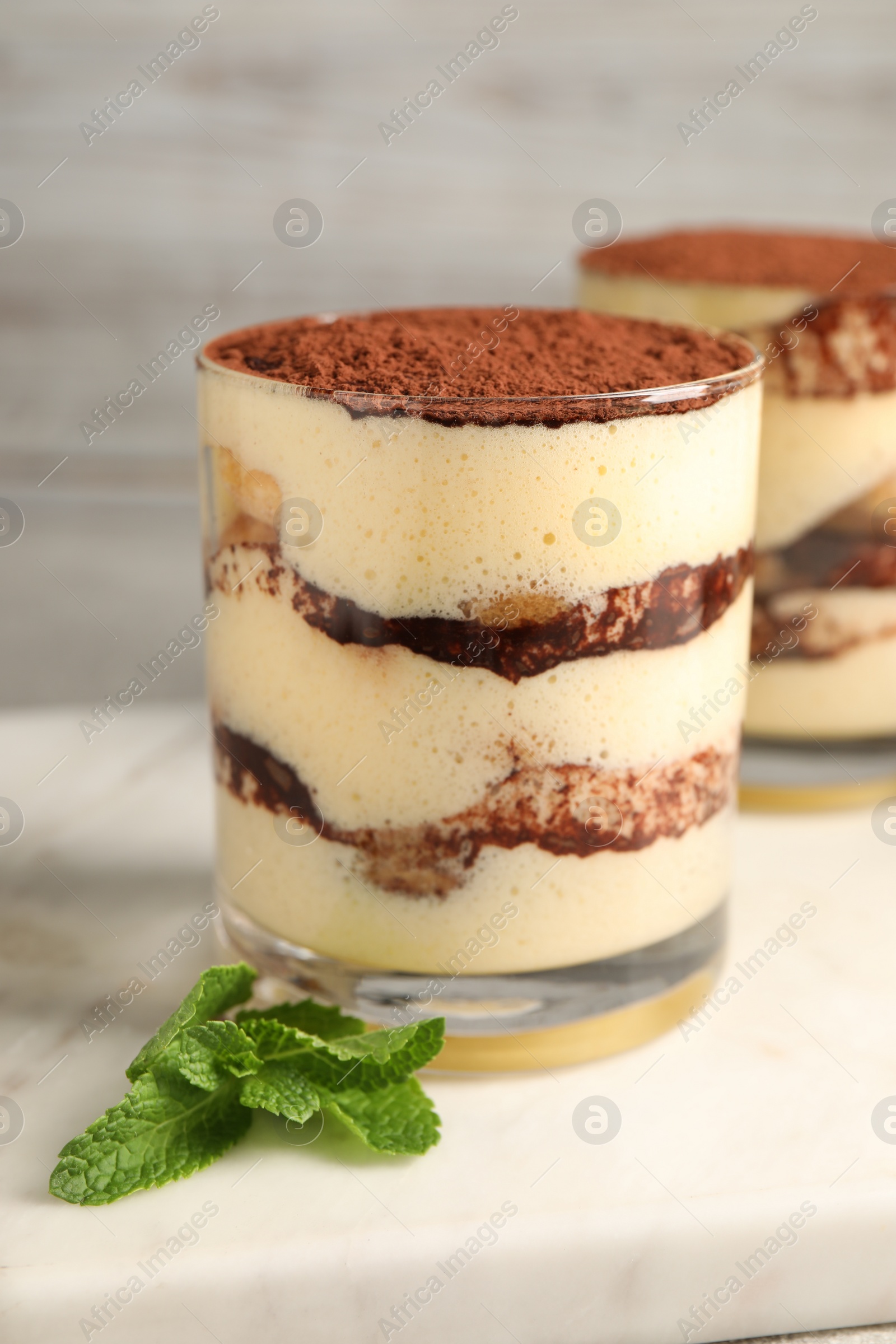 Photo of Delicious tiramisu in glasses and mint on table, closeup