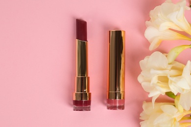 Photo of Bright lipsticks and flowers on pink background, flat lay