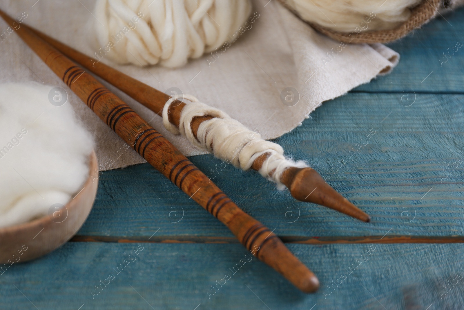 Photo of Soft white wool and spindles on blue wooden table, closeup