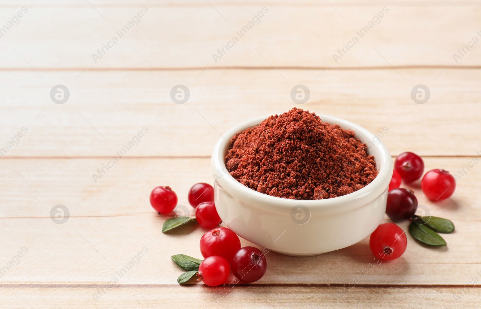 Photo of Dried cranberry powder in bowl, fresh berries and green leaves on light wooden table, closeup. Space for text