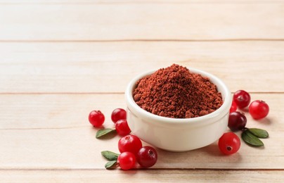 Dried cranberry powder in bowl, fresh berries and green leaves on light wooden table, closeup. Space for text