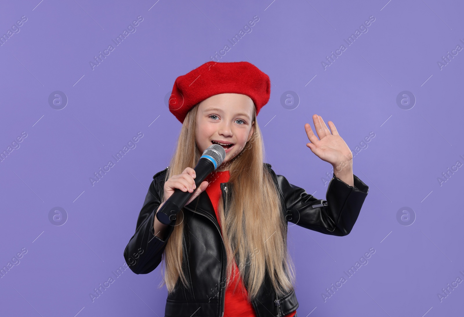 Photo of Cute little girl with microphone singing on purple background