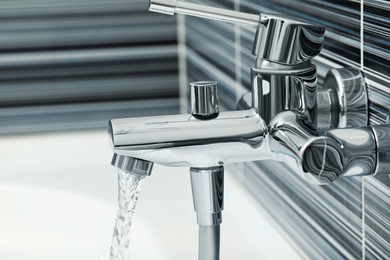 Photo of Water flowing from bath tap installed on black and white wall