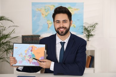 Happy manager showing map at desk in travel agency